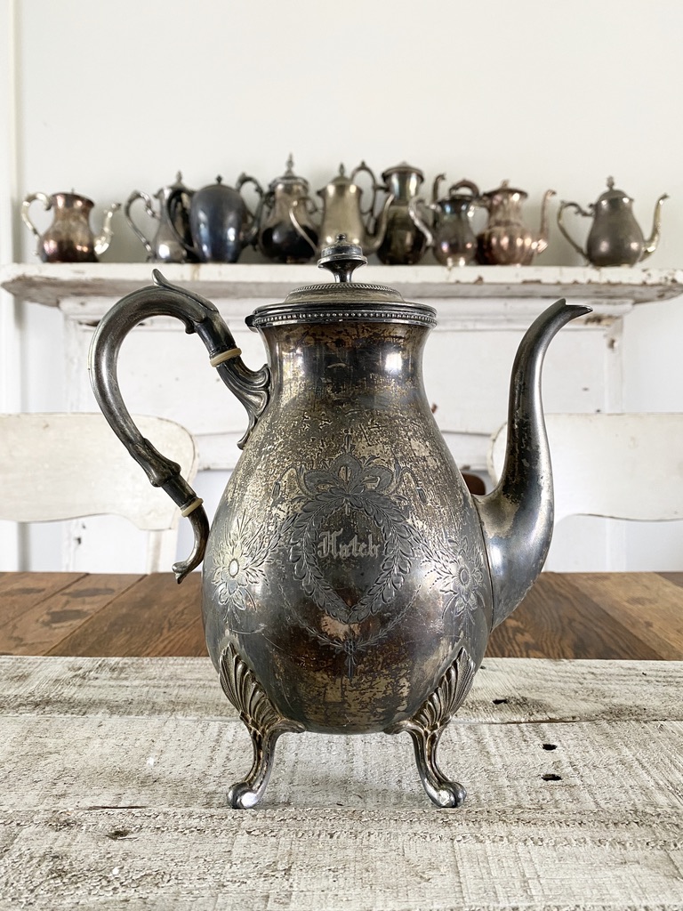 A tarnished vintage silver teapot with an etched flower design and name