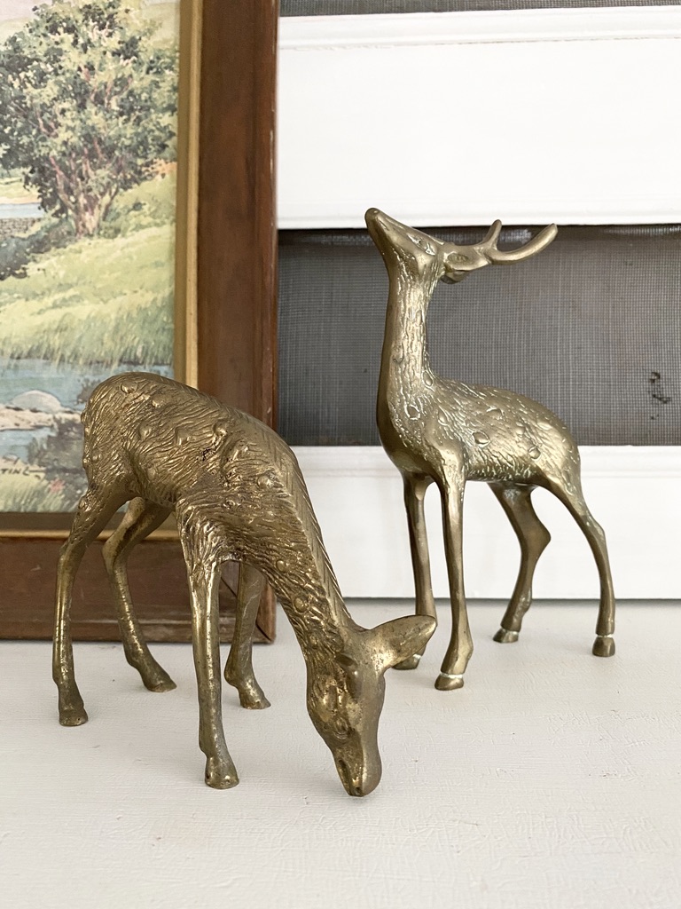 A pair of brass spotted deer on top of an antique white piano