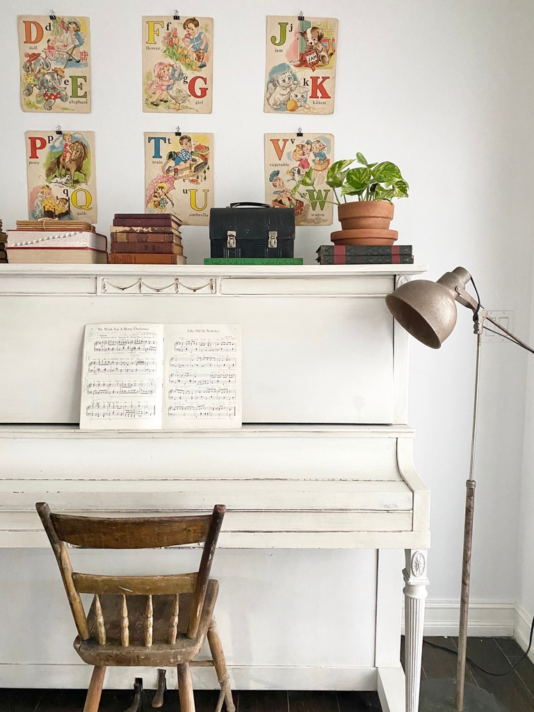 An antique piano styled with vintage book pages, vintage book bundles, and a vintage lunchbox gives back to school vibes