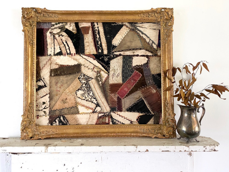 framed quilt on a mantel beside a silver pitcher filled with fall florals