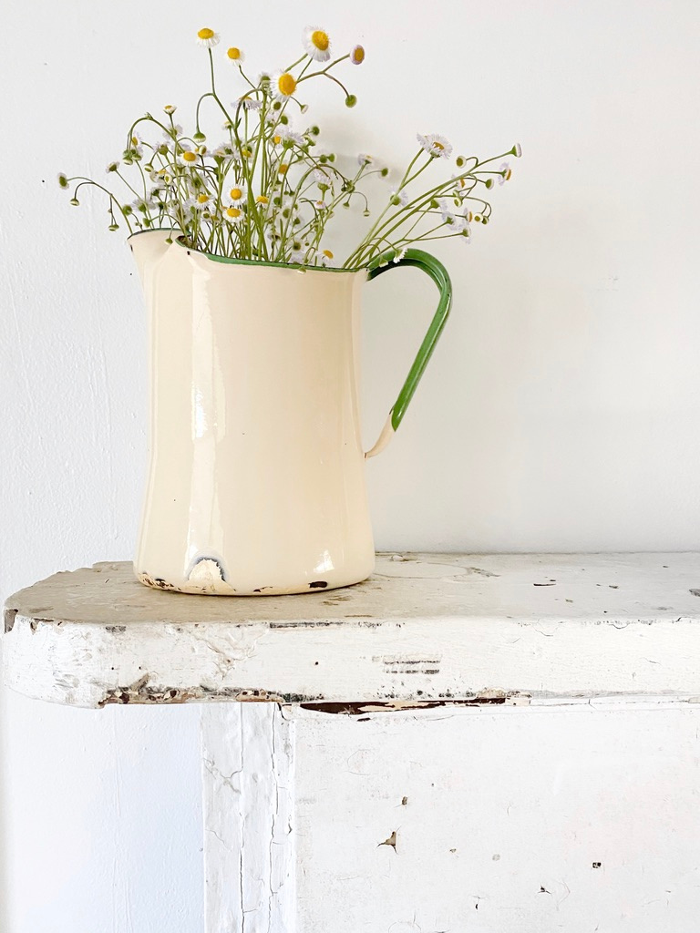 A vintage cream and green enamelware pitcher filled with wildflowers for spring.