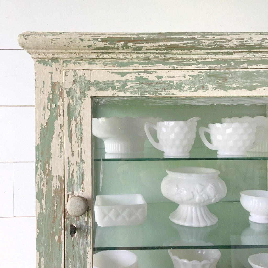Milk glass displayed inside a chippy green cabinet